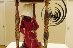 Assembled sculpture of an hourglass , coil, and red and white clothed handmaiden.