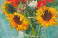 Sunflowers and red flowers in a glass vase against a light blue background.