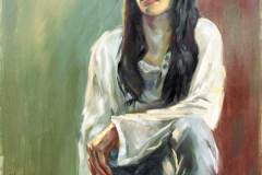 Young woman with dark hair sitting pensively with her arm propped on her knee.