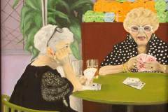 Two older woman playing cards at a green table.