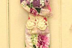 Found object asseblage age of a pink-clad woman in crochet wearing a fish.
