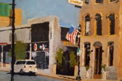 14 – Acrylic painting by J Bowers of street scene focused on an old hotel with an flying American flag.