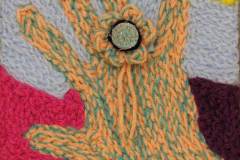 29 an orange and green hand with a floral ring created in thick crochet yarns.
