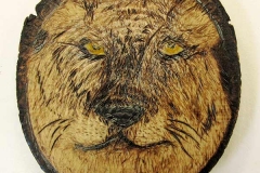 Round disk cut from tree trunk depicting a lion’s head line drawing.