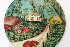 Round disk cut from tree trunk depicting a red car driving up a hill past a red barn towards a church..