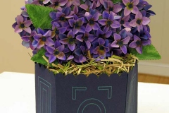 Paper cut work of purple hydrangeas in a blue vase with light green line accents.
