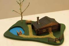 32 - sculpture of a brown log cabin with a path to a tree and pond