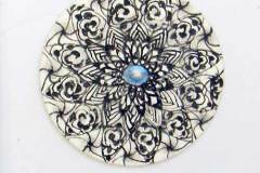 50 - black lines drawing of a round flower shape with a blue jewel in the center