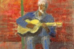 57, a white-haired man in blue playing a guitar underneath a single light.