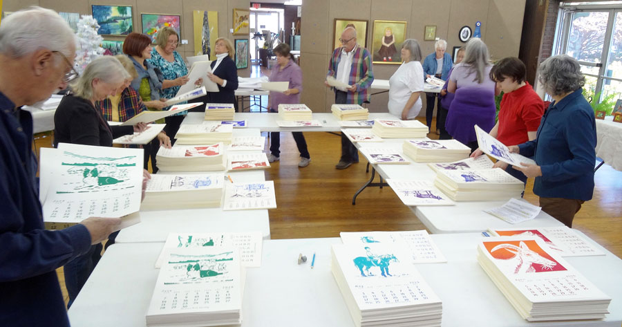 Calendar artists circling table while collating 2020 calendar pages