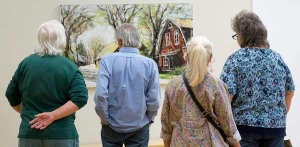 four patrons viewing an oil painting of a red barn amongst spring trees at the Nature Reconsidered 2019 show.
