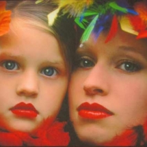 faces of a woman and girl viewed unclose surrounded by brightly colored feathers photographed by Lynne Parker.