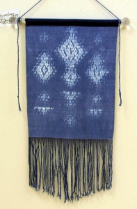 woven fiber art panel of white design on blue background with fringe by Sue Helmken.
