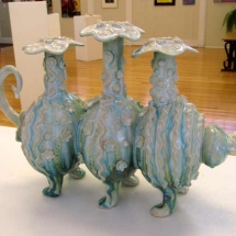 whimsical pottery work of 3 jugs that form a cat with 6 legs, covered in floral shapes and stripes by artist Renee Matthews.