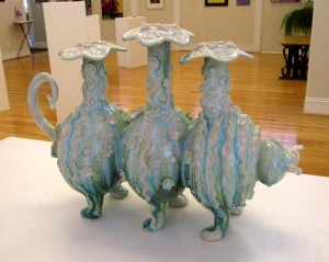 whimsical pottery work of 3 jugs that form a cat with 6 legs, covered in floral shapes and stripes by artist Renee Matthews.