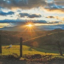 Appalachian field below a sunset behind the mountain range photographed in color by photographer Robert Webb.