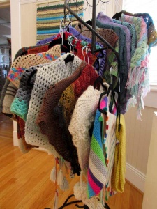 rack of multiple, multi-colored hand-knitted shawls.