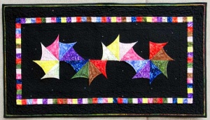 Multi-colored pinwheel stars and beads on a black background patchwork quilt by artist Carol McLaughlin.