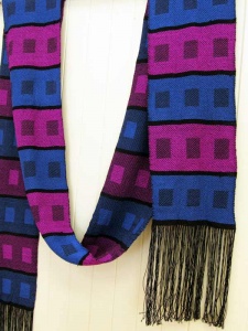Woven blue, purple, black and magenta striped and box-shaped designs on scarf with fringe by artist Chris Dunlap.