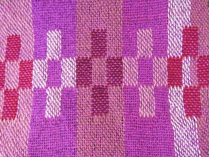 Enlarged detail of woven pink and magenta striped and box-shaped designs on 2 scarves with fringe by artist Chris Dunlap.