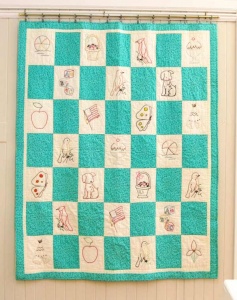 Blue and cream checkered patchwork quilte with embroidered line drawings of animals and food by artist Karen Kuhl.