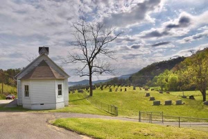 43 small rural house in front of rolling hillside cemetary under a wide skyline.