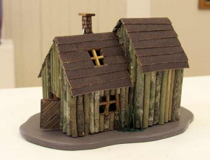 Sculpture of house made of green and brown sticks.