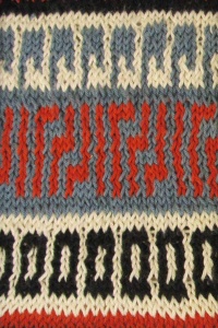 Blue-gray knitted art with black, red and geometric shapes.