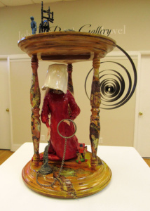 Assembled sculpture of an hourglass , coil, and red and white clothed handmaiden.