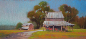 Rural scene of 2 decaying barns on a curved roadside with trees in the background.