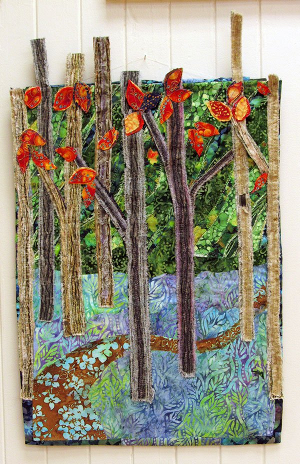 Textile hanging artwork of woven apllique-quilt forest scene of tall trees with fall red leaves.