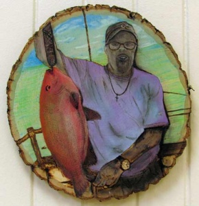 an african american man holding up his fishing catch - all engraved and painted on a disc from a real tree.