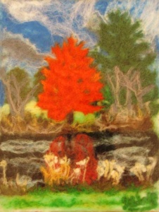 fuzzy thread rendering of a bright red tree between brown and green trees in a clearing.