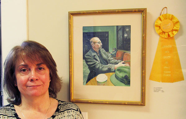 Artist next to her color pencil drawing of a manin a winter coat sitting in a near-empty coddeeshop, with his cup and fedora hat in the foreground.