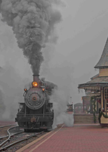 Photography of a frontal view of old train engine 40 emerging from a dark gray veil of smoke.
