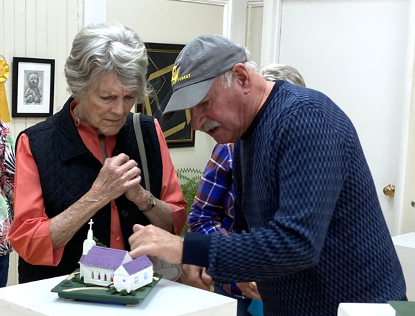 artist Alez Pietersen shows his miniature church model to a gallery visitor