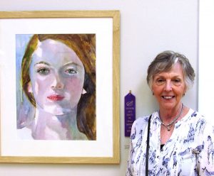 artist Lynn Schilling in front of merit award winning watercolor portrait of a woman